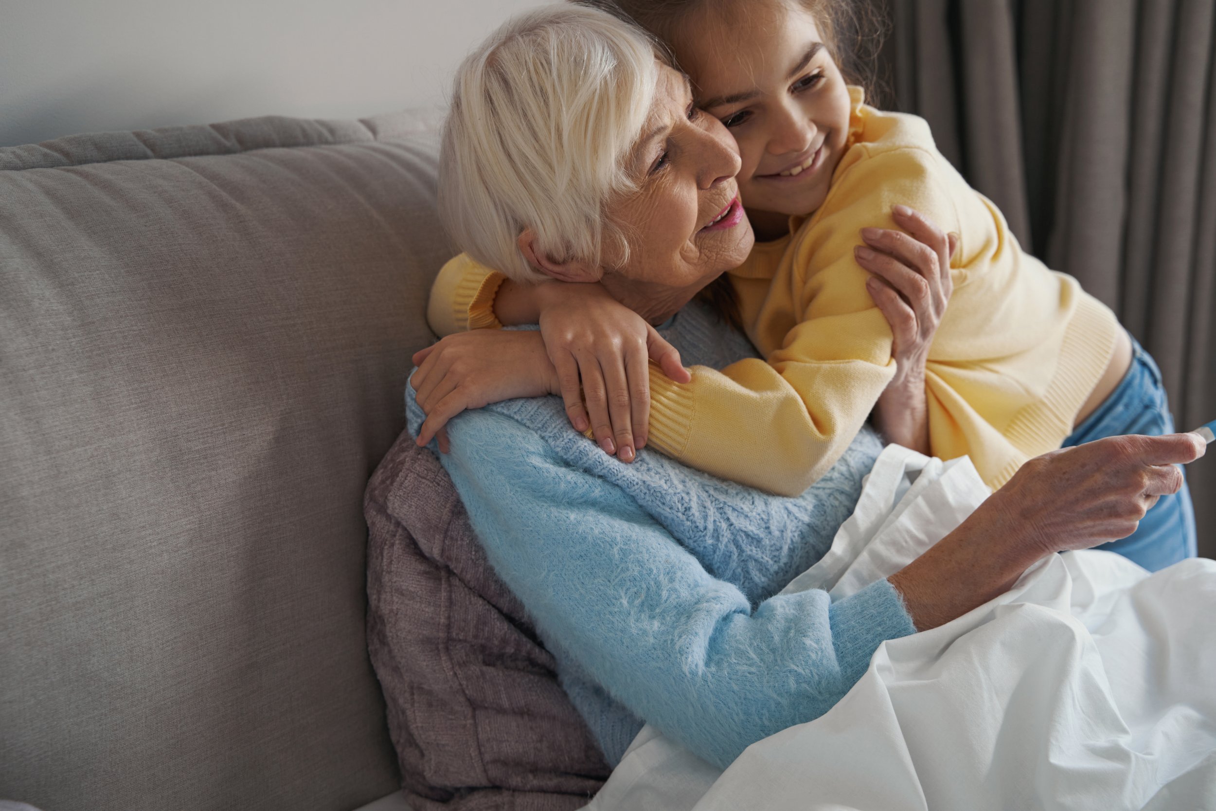 Close-up photo of adorable little girl smiling and hugging her bedridden grandma